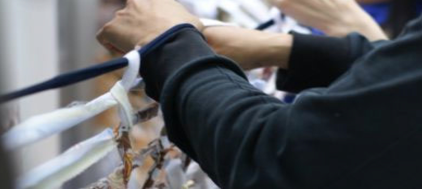 Close-Up-Fotografie von einer Person, von der nur die Hände und Arme in einem schwarzen Pullover zu erkennen sind, die Stoffstücke an eine schwarze Stoffleine binden.