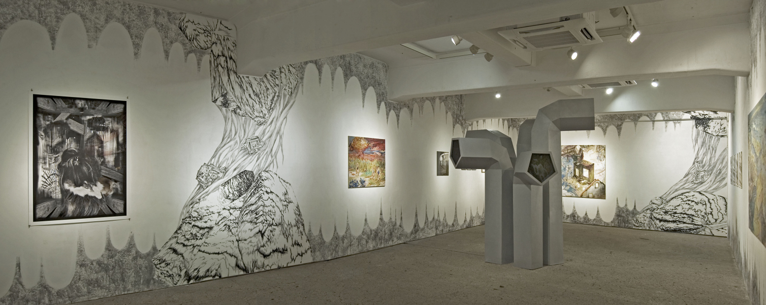 View of an exhibition in a windowless room. In the middle of the room is an installation of five grey objects of different sizes, reminiscent of giant ventilation pipes. There are several paintings on the walls. The walls themselves are also painted in black and white with different motifs.