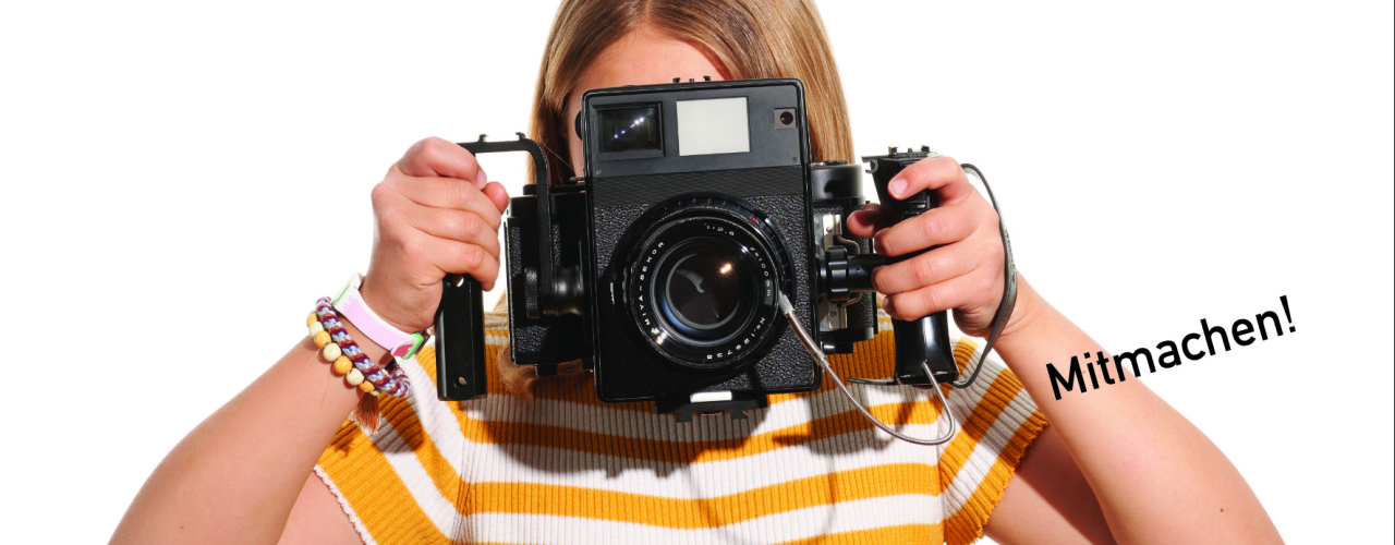 A young girl in front of a white background holds a camera in front of her eyes