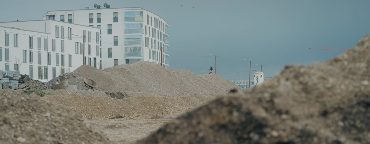 Das Bild zeigt die Baustelle mit Erdaushub und bereits fertige Wohnblocks