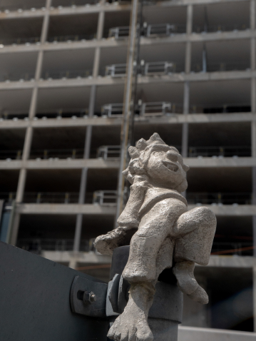 Pumuckl sits on a street sign, with a high-rise construction site in the background