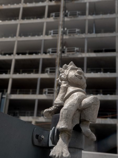 Pumuckl sitzt auf einem Straßenschild, im Hintergrund Hochhaus-Baustelle