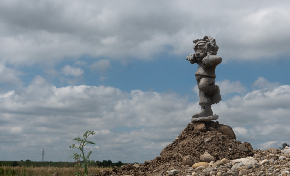 A Pumuckl sculpture stands on top of a mound of earth on a building site