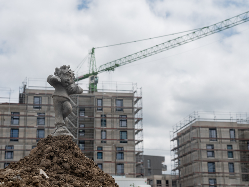 Pumuckl sticks out his tongue and stands on one leg on a construction site mound