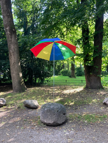 Photograph taken in the Old Botanical Garden. An open, colourful parasol is inserted into a roundish stone.