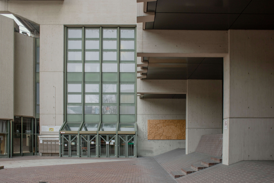 Photograph of the entrance to the criminal justice centre on Nymphenburger Straße. You can see the green glass entrance to the grey exposed concrete building from the 1970s and the paved forecourt in front of the building.