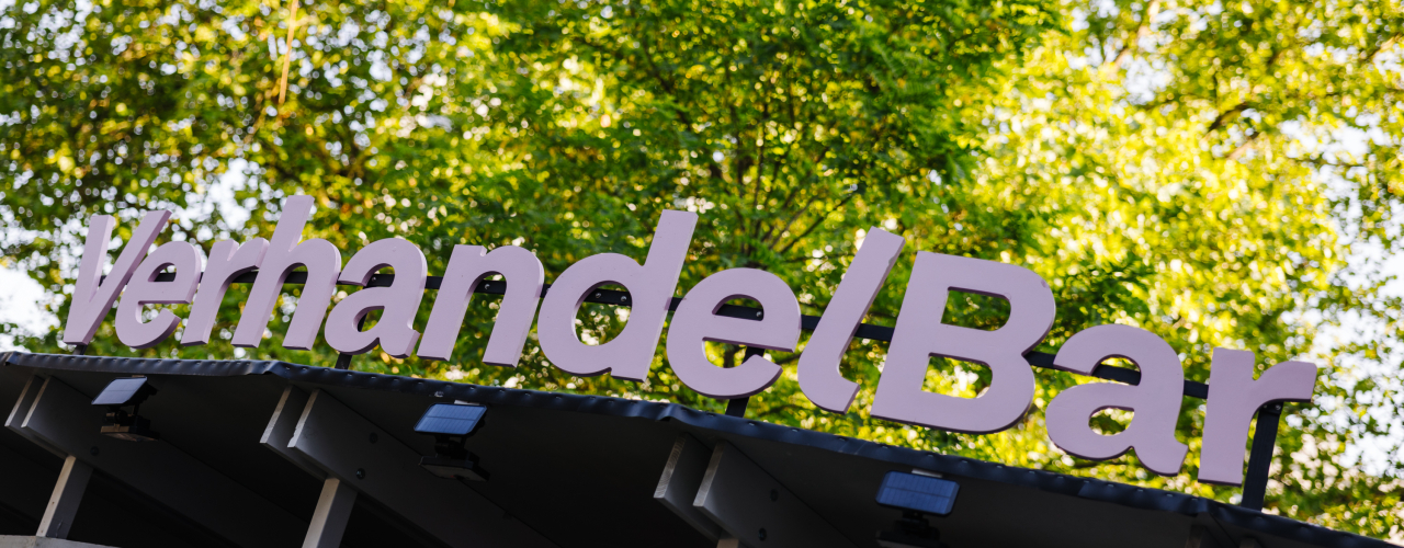 VerhandelBar lettering in pink letters on a simple timbered roof, trees in the background