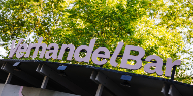 VerhandelBar lettering in pink letters on a simple timbered roof, trees in the background