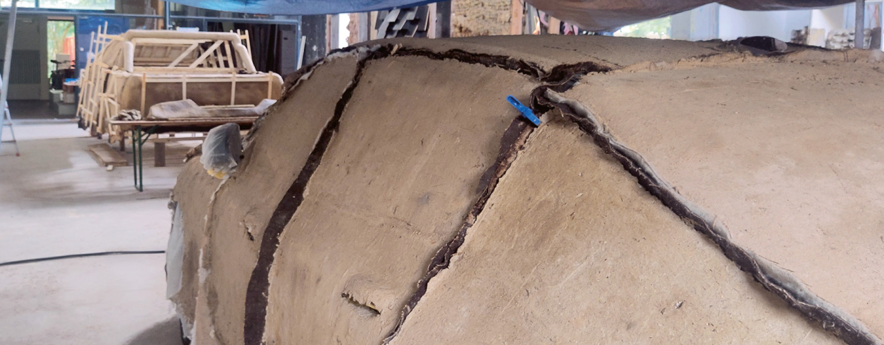 View of a compostable SUV during production. A loamy mass is applied to a wooden frame.