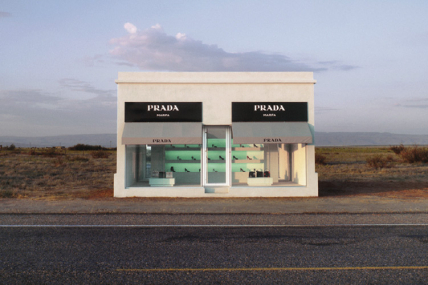 Das Bild zeigt eine einsame Prada-Boutique in einer Wüstenlandschaft, direkt an einer Straße, umgeben von leerer, trockener Natur.