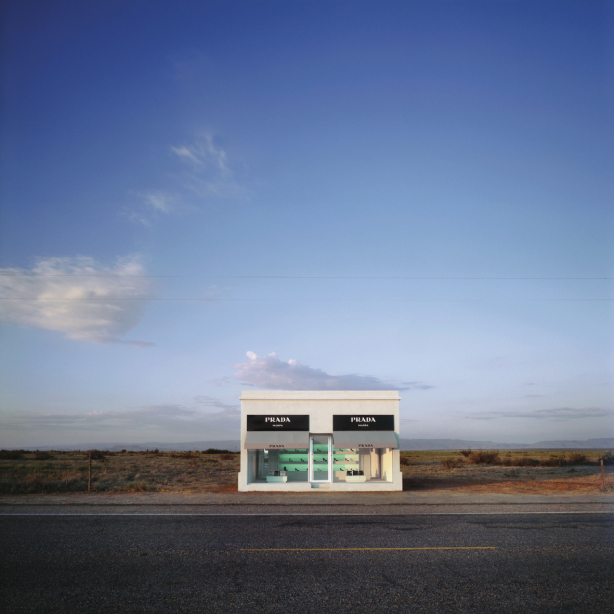 The image shows a solitary Prada boutique in a desert landscape, located by a road and surrounded by empty, dry nature.