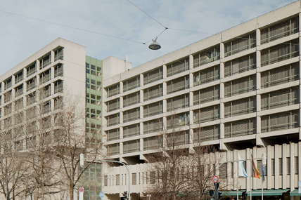 Fotografie des Strafjustizzentrum an der Nymphenburger Straße. Zu sehen ist der graue Sichtbetonbau aus den 1970er Jahren sowie die Straßenkreuzung vor dem Gebäude.