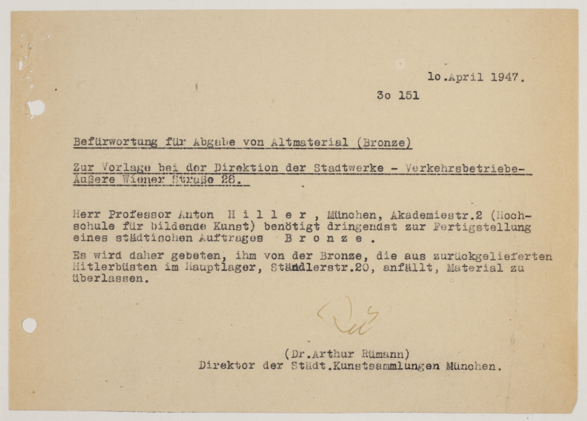 Ein historisches Dokument vom 10. April 1947 auf vergilbtem Papier über die Befürwortung für Abgabe von Altmaterial (Bronze). Mit Schreibmaschine geschrieben: Dr. Arthur Rümann, damaliger Direktor des Lenbachhauses befürwortet schriftlich, Herrn Professor Anton Hiller die Abgabe von zurückgelieferten Hitlerbüsten aus Bronze im Hauptlager der Städtischen Straßenbahnbetriebe.